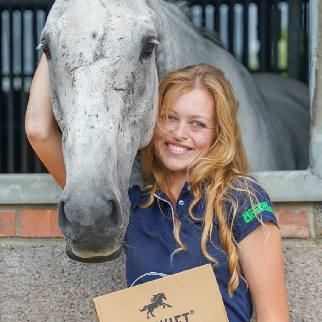 Smiling woman with a gray horse in a stable holding a Pet Jet Co. box – premium horse grooming and care products